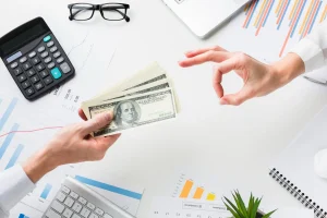 Empresario recibiendo capital de trabajo en efectivo sobre escritorio con gráficos financieros y calculadora